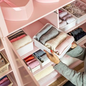Woman organizing neatly folded clothes in a pink closet with white bins